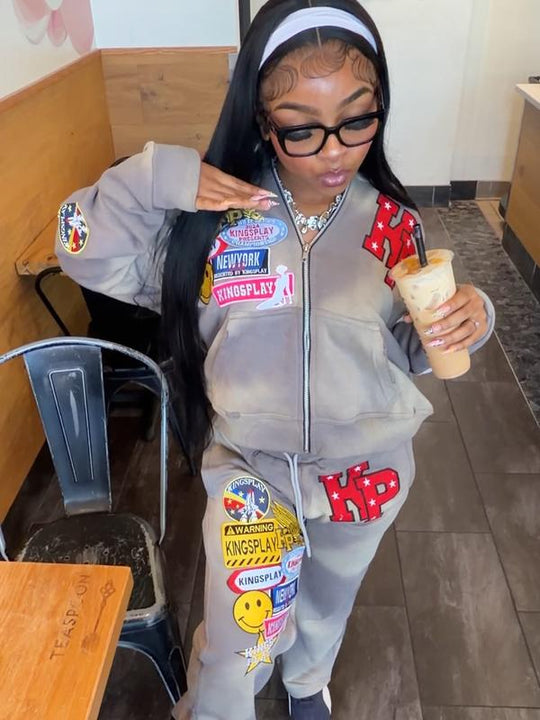 Customer wearing the Ash K1 Tracksuit, matching taupe jacket and sweatpants with red KP patches, holding an iced drink in a boba shop.