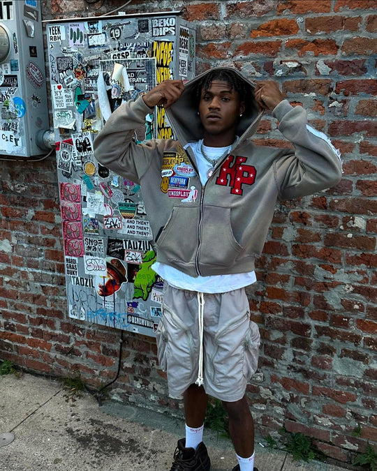 customer in the ash k1 zip up with the hood up against a sticker-covered brick wall