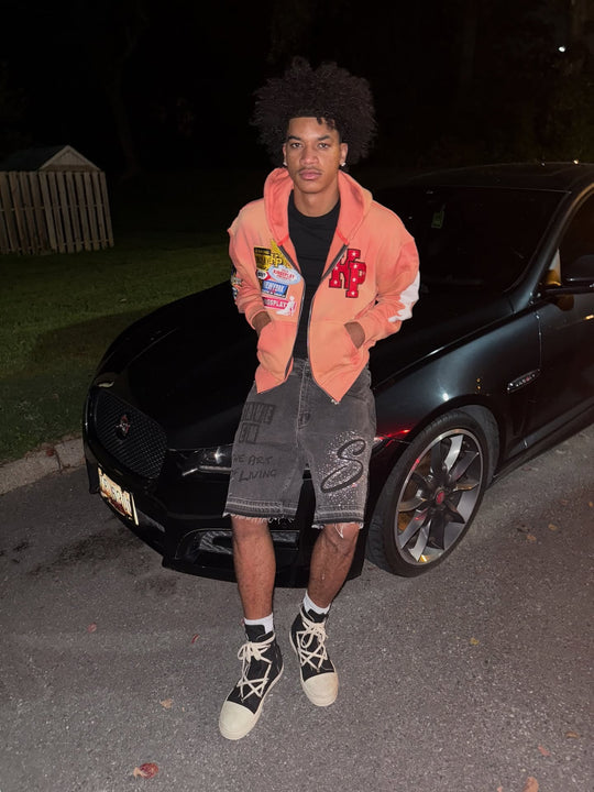 customer in the peach k1 zip up and distressed denim shorts by a black jaguar at night