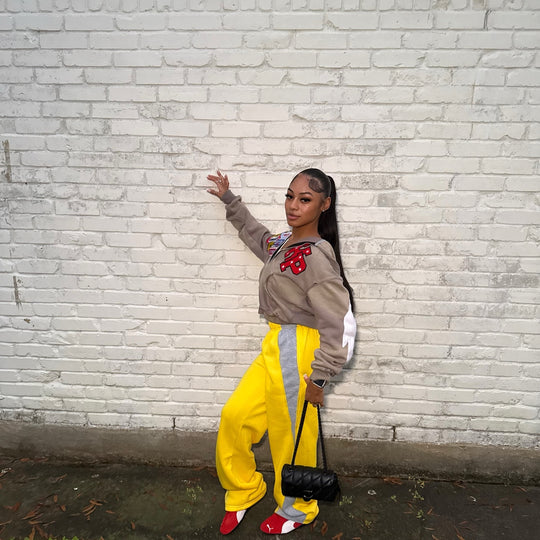 customer in the cropped ash k1 zip up and yellow track pants at a white brick wall