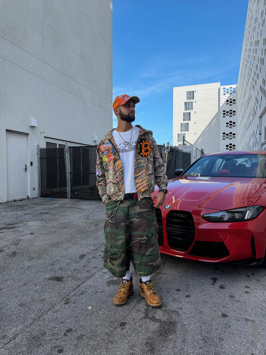 customer in the bitcoin camo k1 zip up and camo cargos beside a red bmw