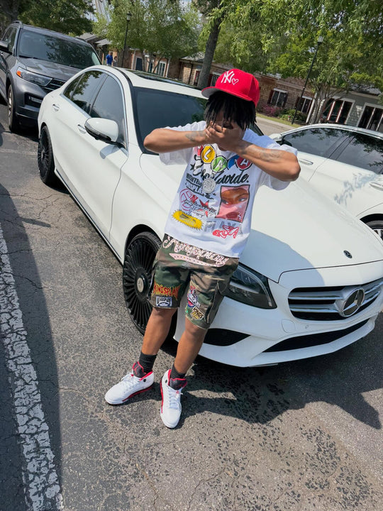 customer in the global tee and patched up camo jorts leaning on a white mercedes