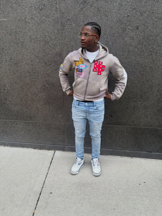 customer in the ash k1 zip up and light-wash jeans against a concrete wall